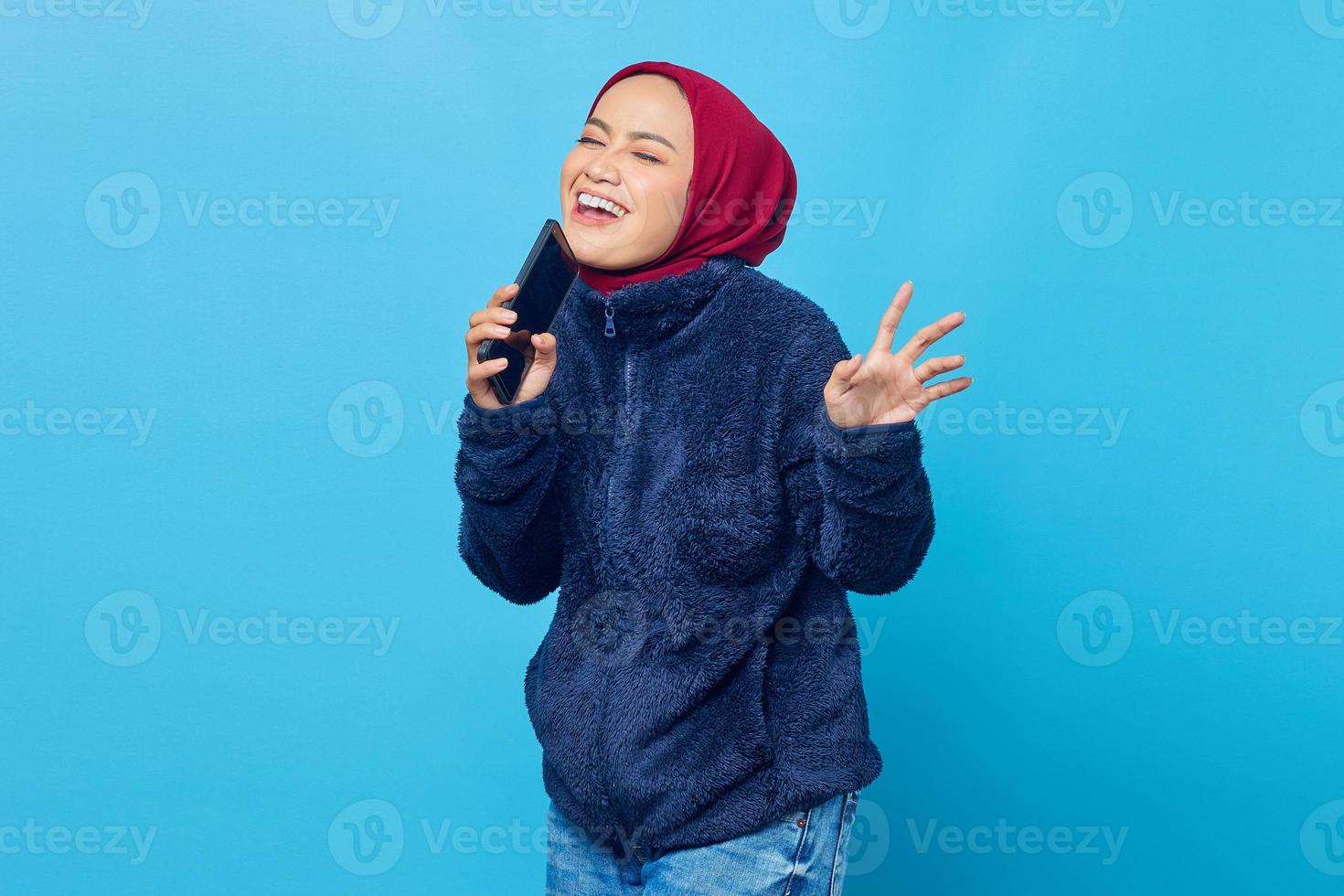 linda mulher asiática curtindo cantar usando o smartphone sobre fundo azul foto