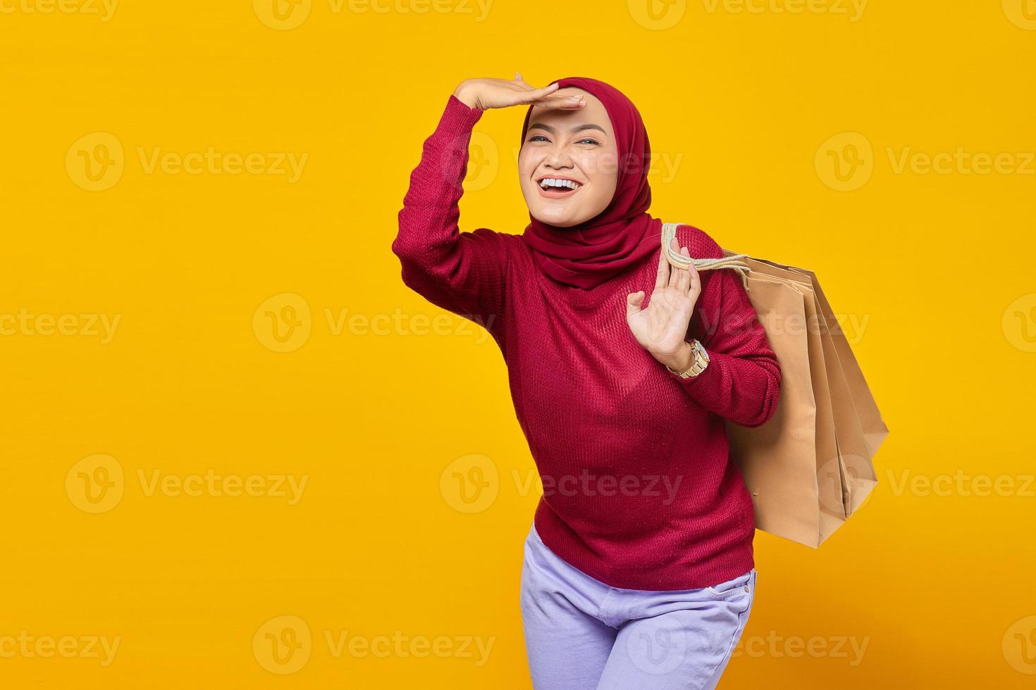 mulher asiática jovem e alegre, animada e segurando sacolas de compras no fundo amarelo foto