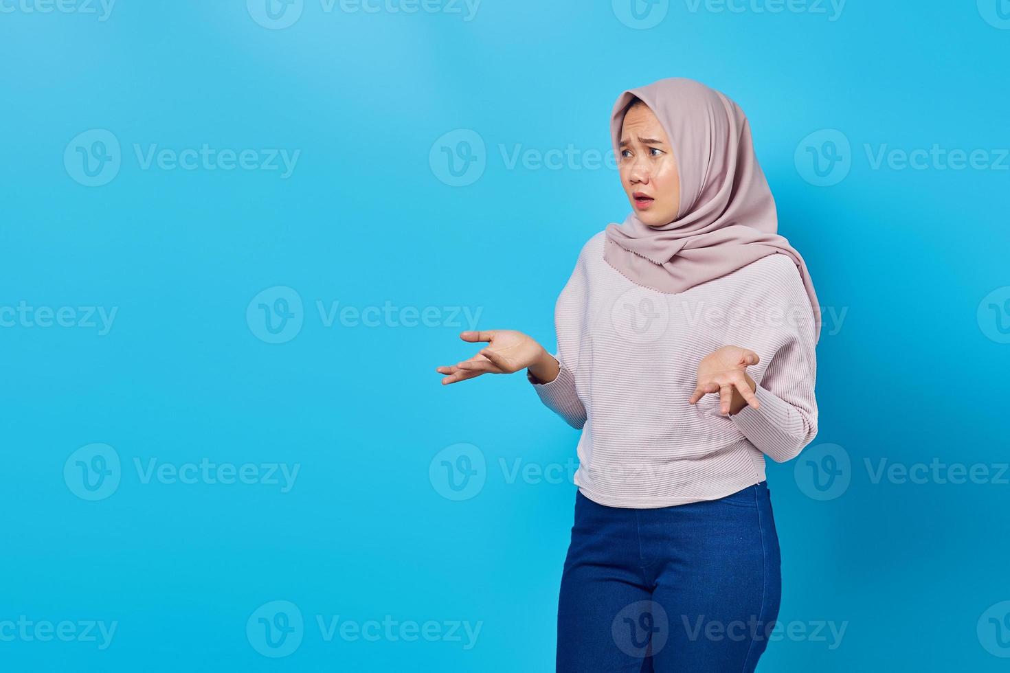 retrato de uma linda mulher asiática surpresa com uma expressão de confusão e desagrado no fundo azul foto