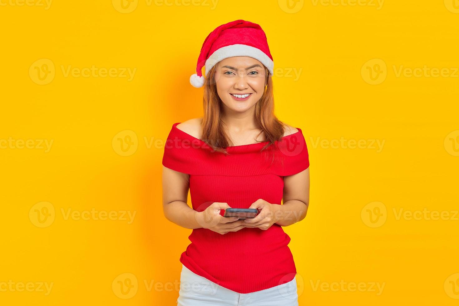 retrato de uma jovem alegre usando o Natal usando o smartphone em fundo amarelo foto