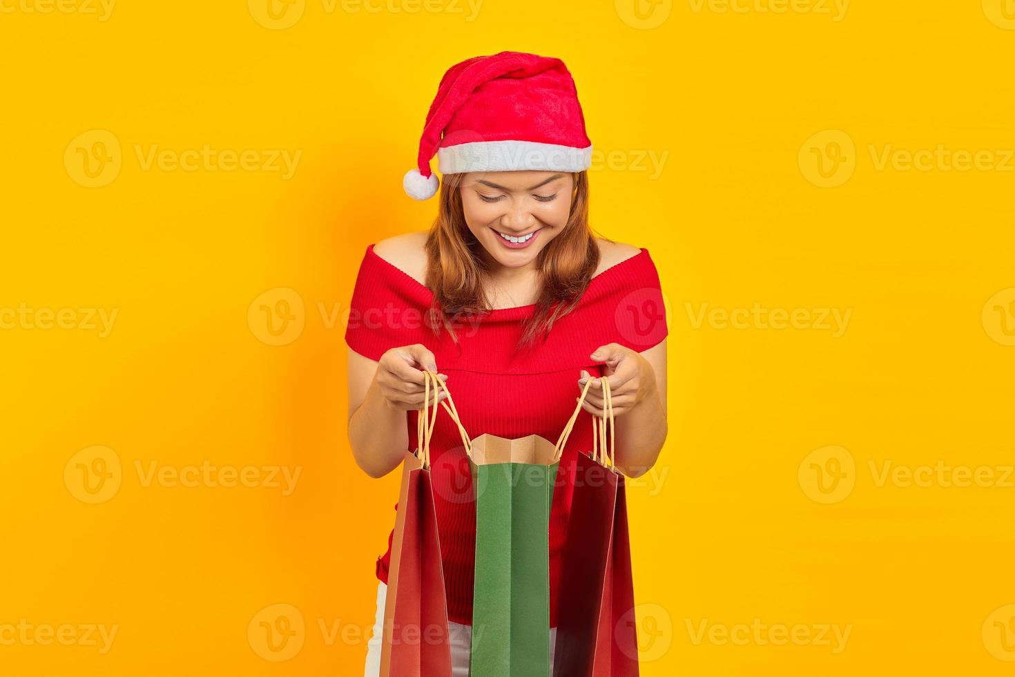 sorridente jovem asiática abrindo e olhando dentro da sacola de compras em fundo amarelo foto