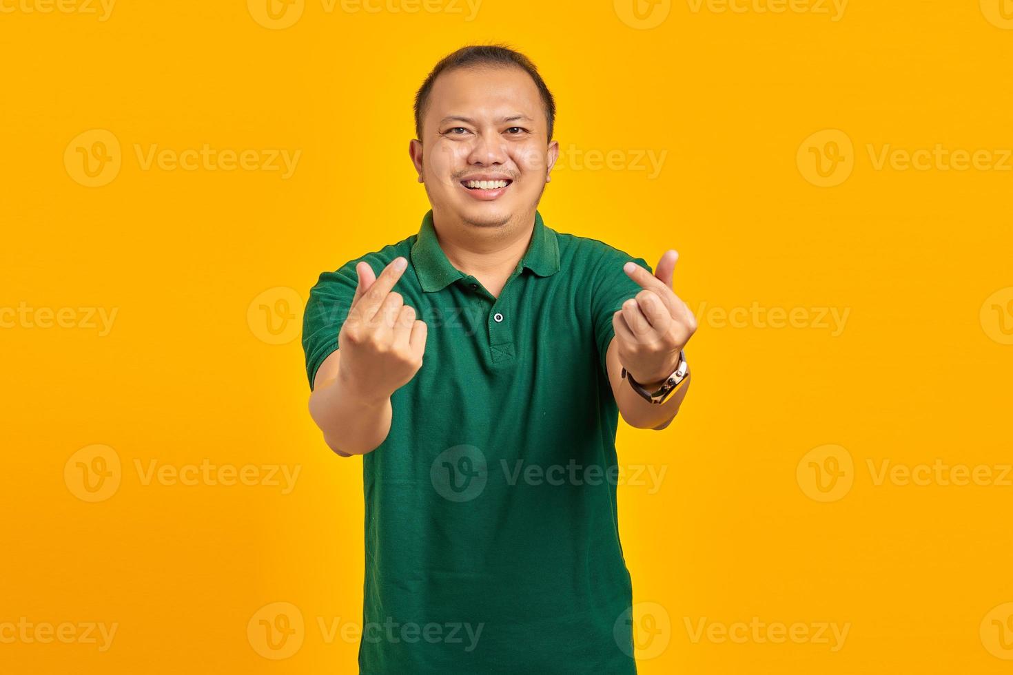 retrato de jovem asiático alegre mostrando coração de dedo sobre fundo amarelo foto