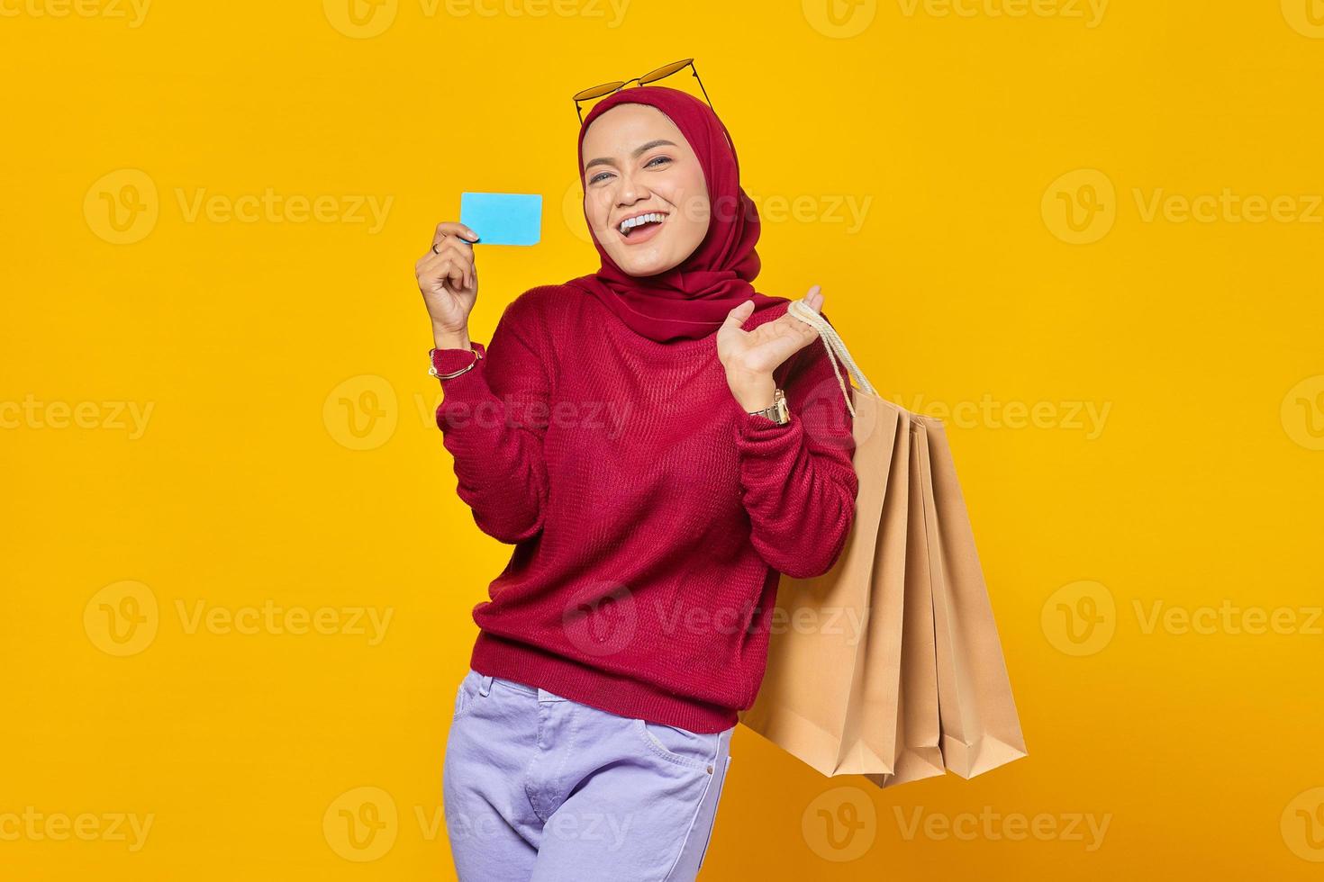 retrato de uma mulher asiática alegre segurando uma sacola de compras e mostrando o cartão de crédito sobre fundo amarelo foto