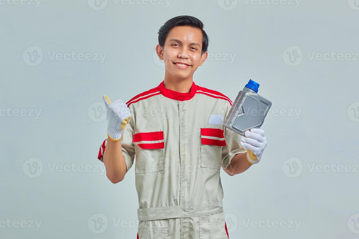 retrato de um homem bonito sorridente, vestindo uniforme de mecânico, mostrando a garrafa de plástico de óleo de motor e apontando para o espaço vazio sobre um fundo cinza foto