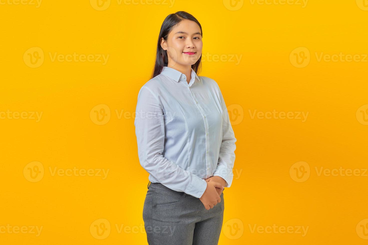 Mulher de negócios jovem bonita sorridente de mãos dadas com rosto confiante em fundo amarelo foto