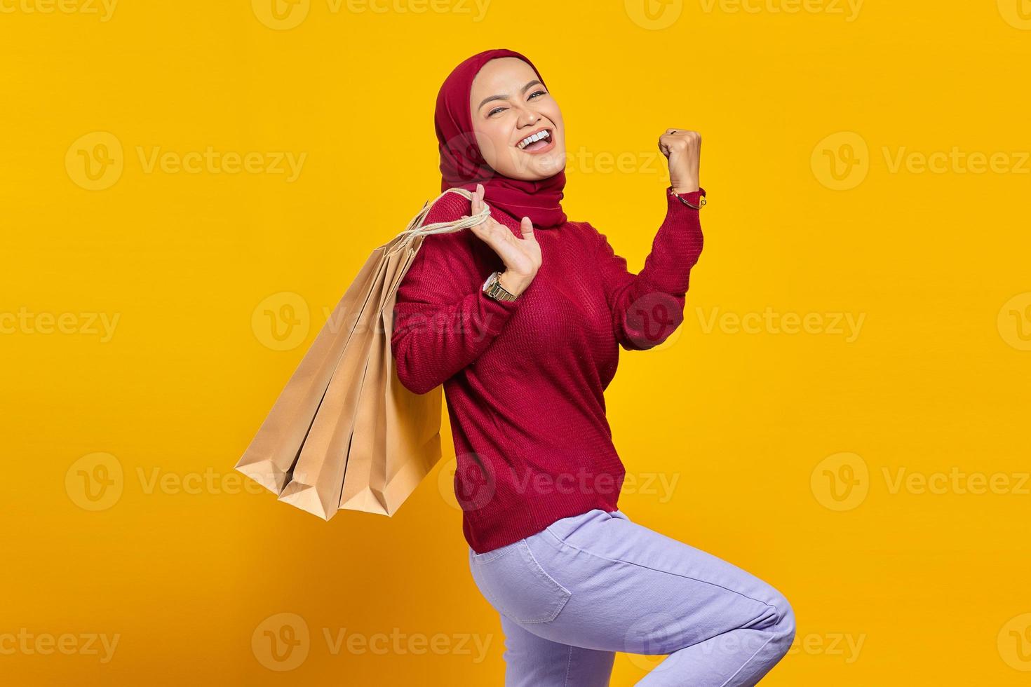 animada e alegre jovem asiática segurando sacolas de compras em fundo amarelo foto