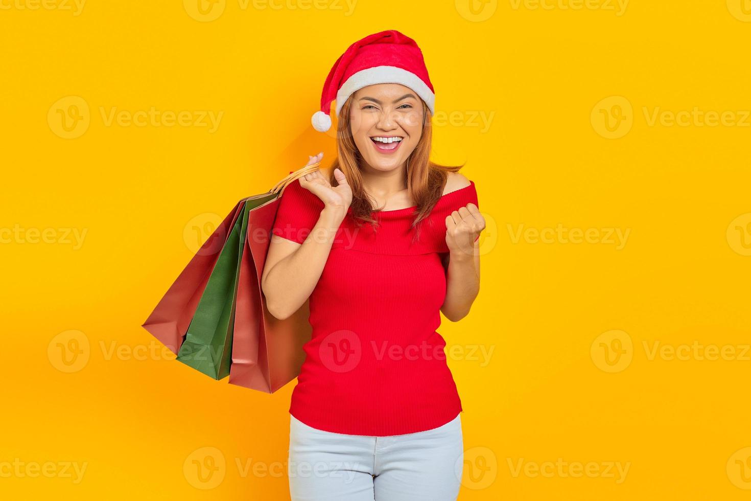 jovem alegre com chapéu de Papai Noel segurando sacolas de compras e comemorando a satisfação das compras foto