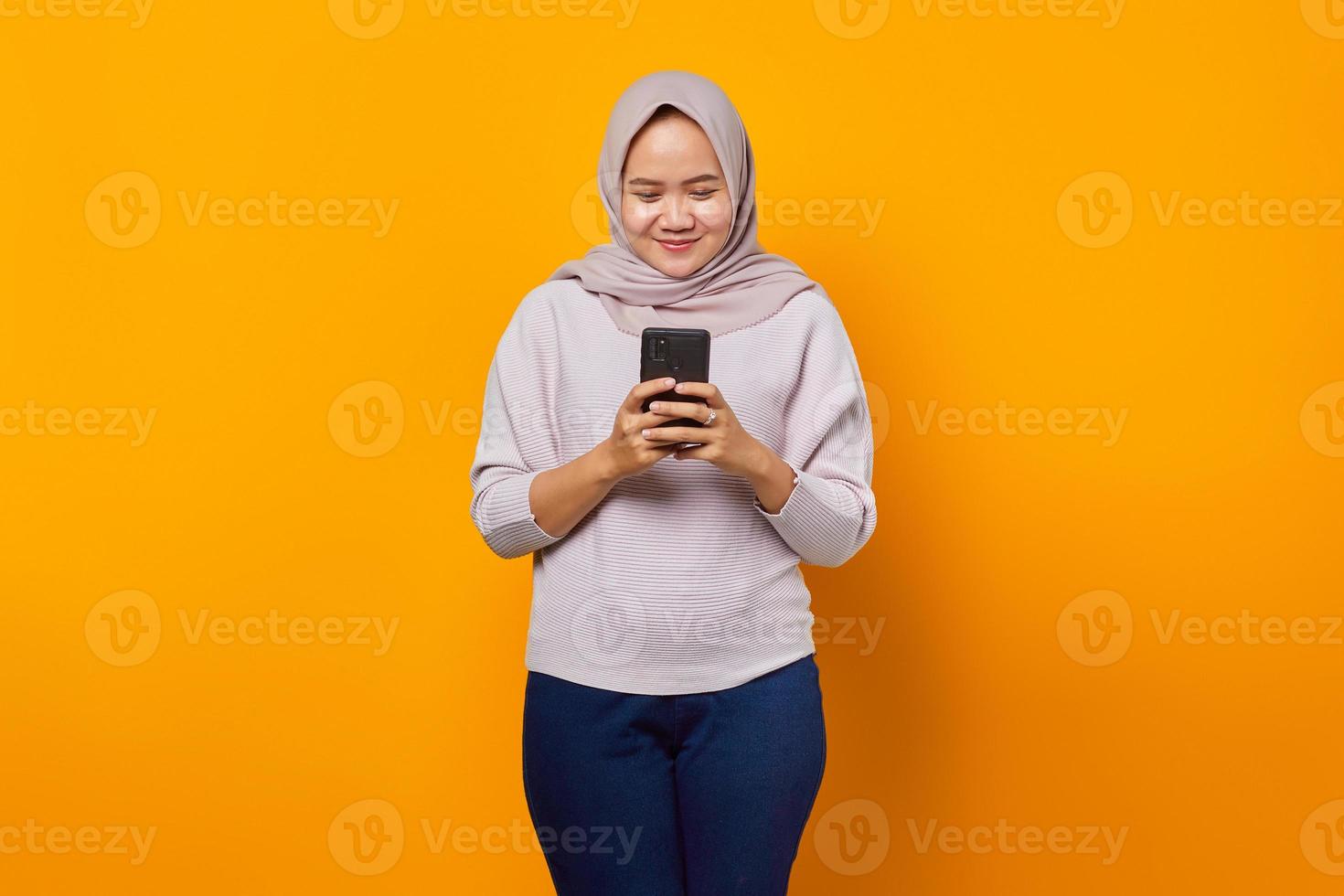 retrato de mulher asiática atraente e alegre usando telefone celular sobre fundo amarelo foto