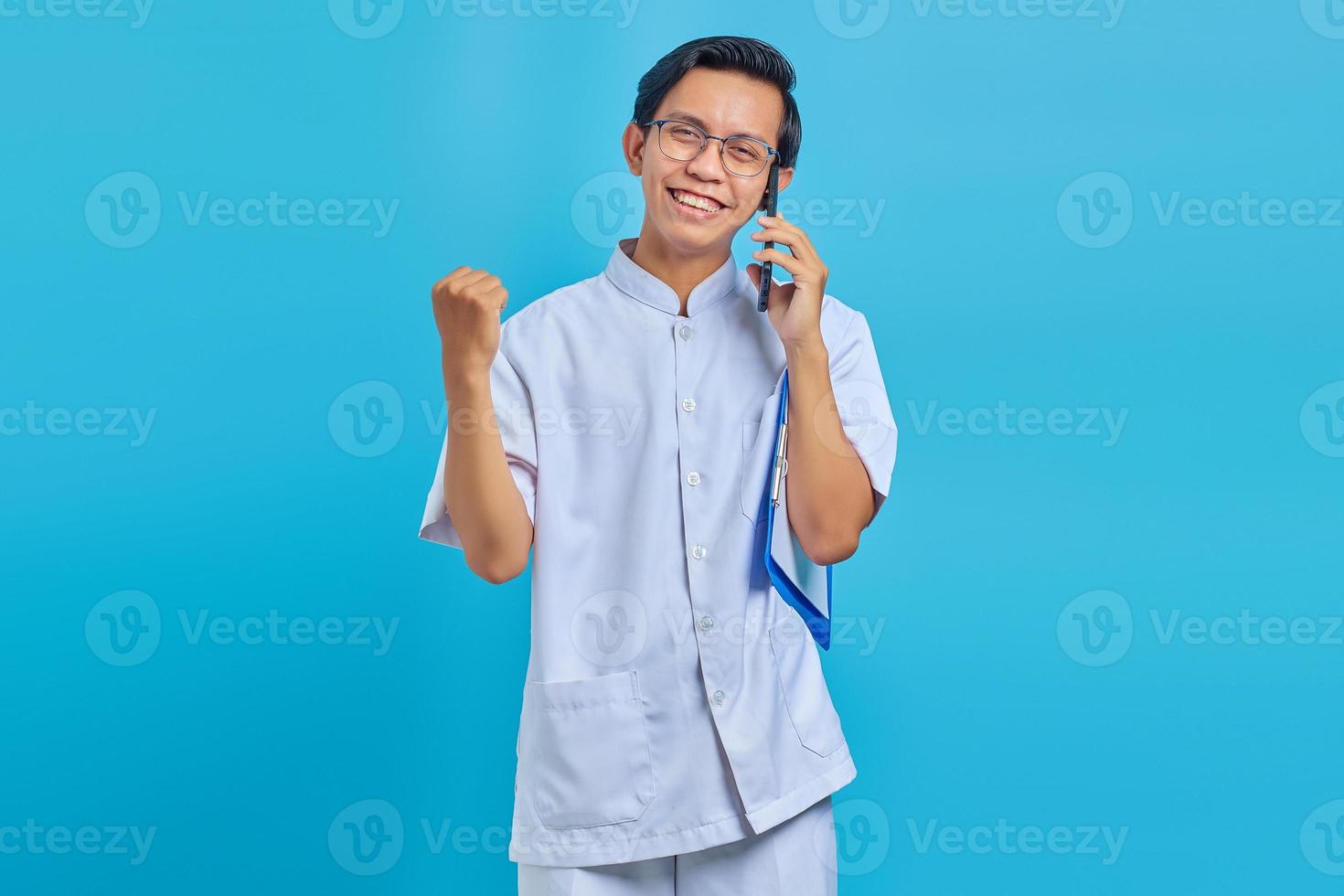 alegre bonito enfermeiro segurando uma prancheta e falando no celular sobre fundo amarelo foto