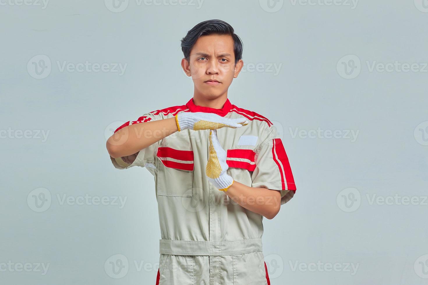 retrato de homem bonito vestindo uniforme mecânico mostrando gesto de tempo limite em fundo cinza foto