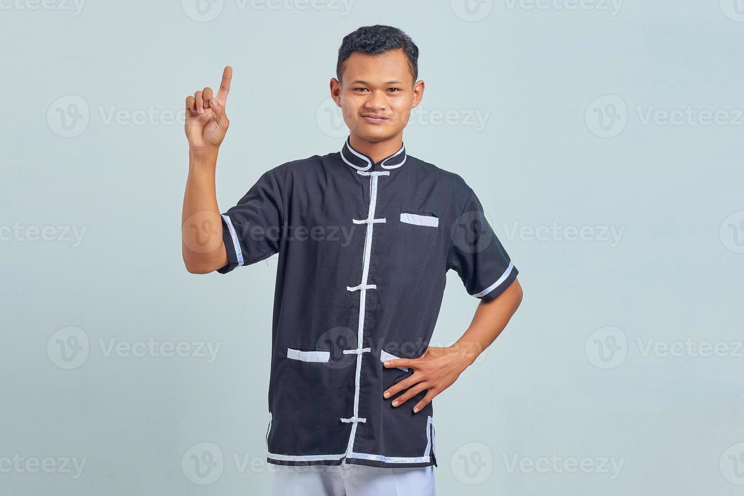 retrato de jovem asiático animado vestindo quimono taekwondo, levantando o dedo e tendo uma ideia criativa isolada em fundo cinza foto