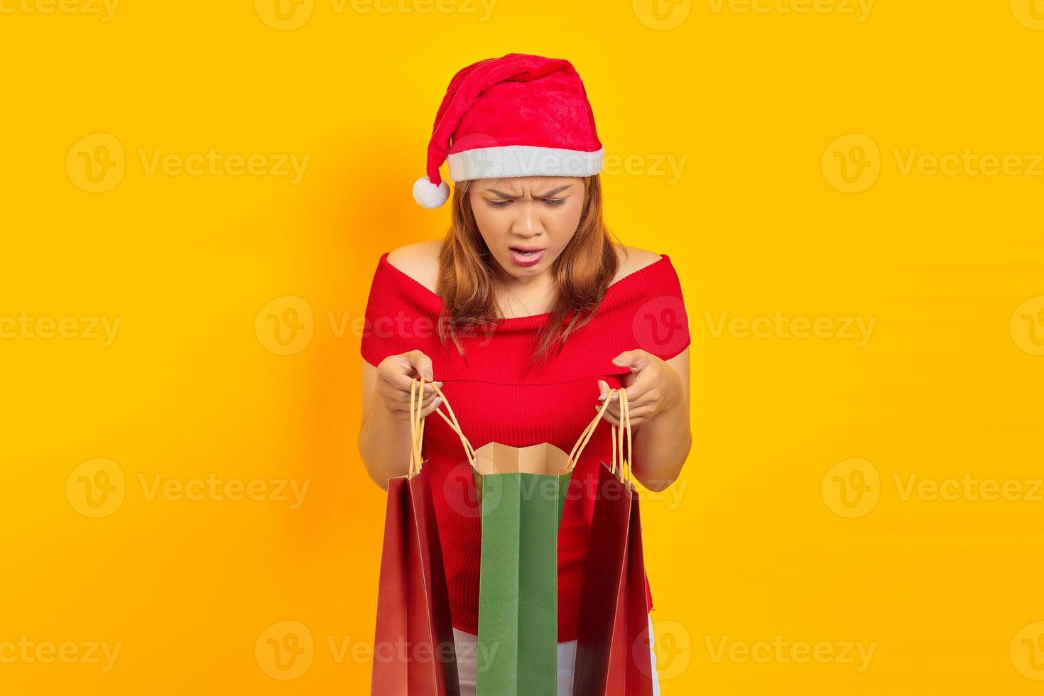 Surpreendeu a jovem asiática abrindo e olhando dentro da sacola de compras com a boca aberta, isolada em um fundo amarelo foto