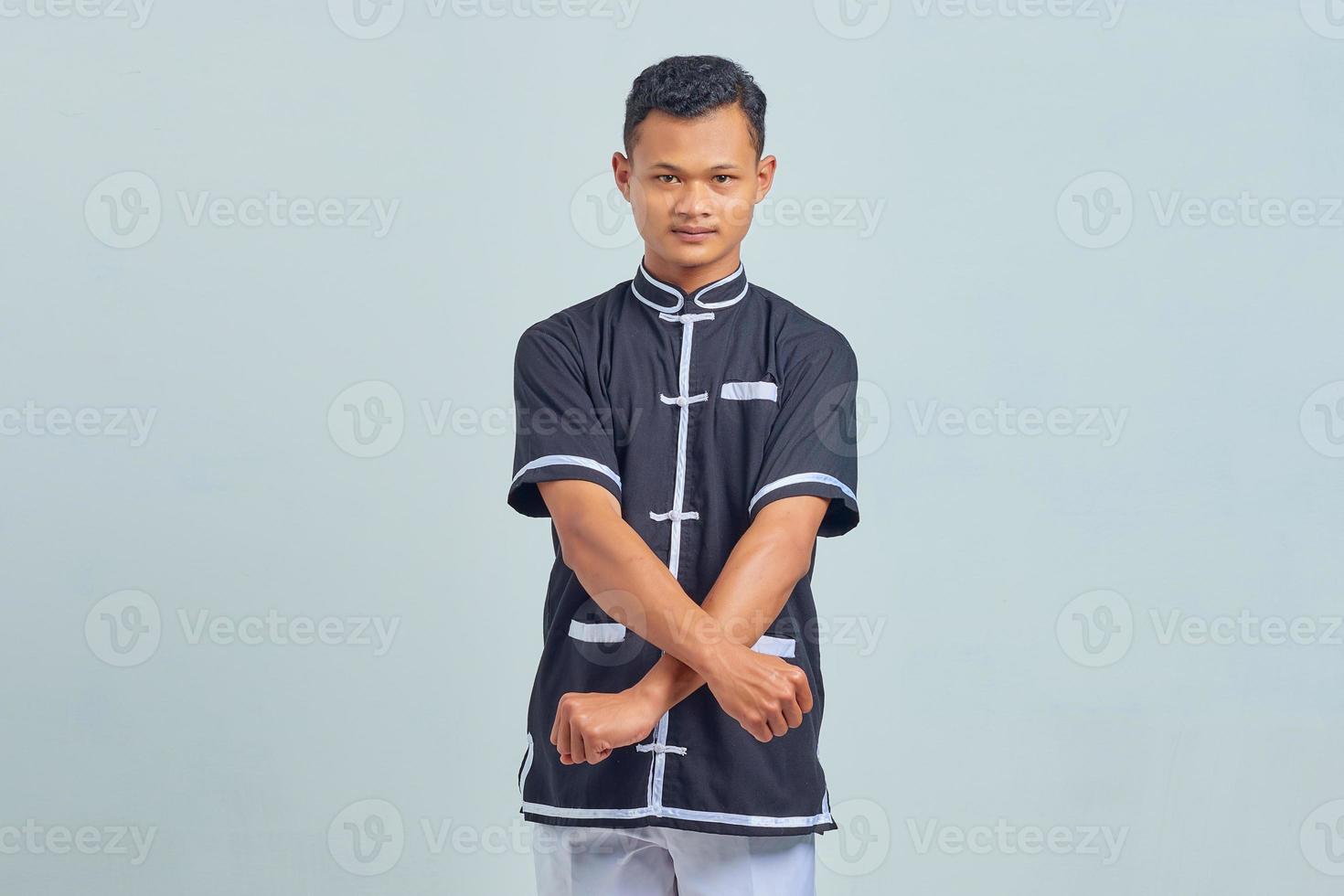 retrato de jovem asiático vestindo quimono taekwondo mostrando gesto de boxeador sobre fundo cinza foto