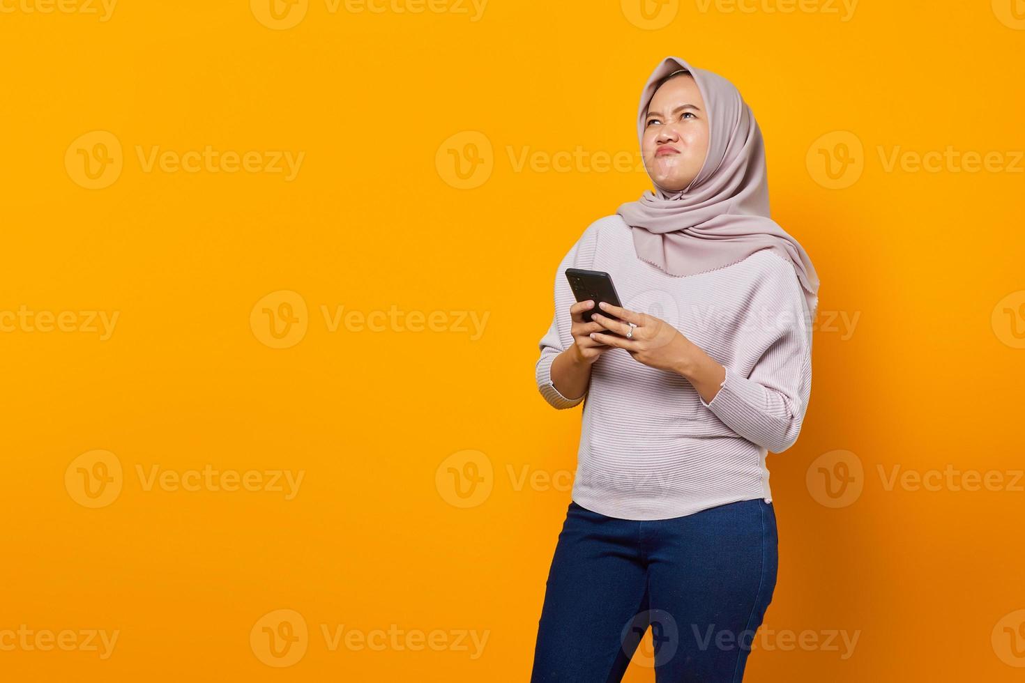 retrato de uma linda mulher asiática segurando um telefone celular e olhando de lado no fundo amarelo foto