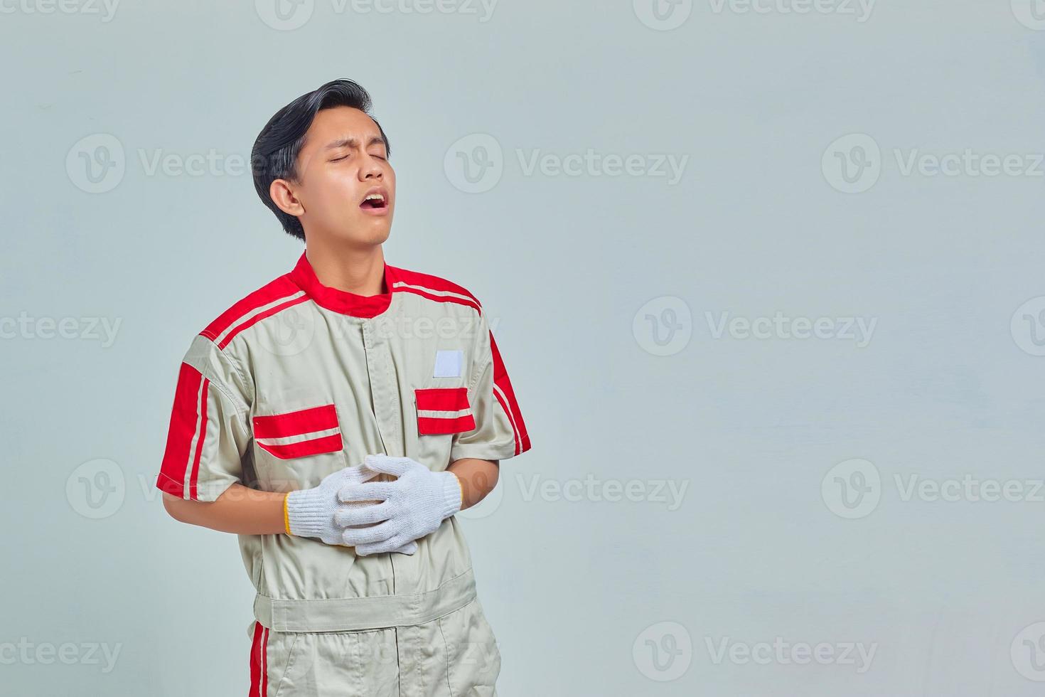 retrato de bonito mecânico com dores com a mão na barriga em fundo cinza foto