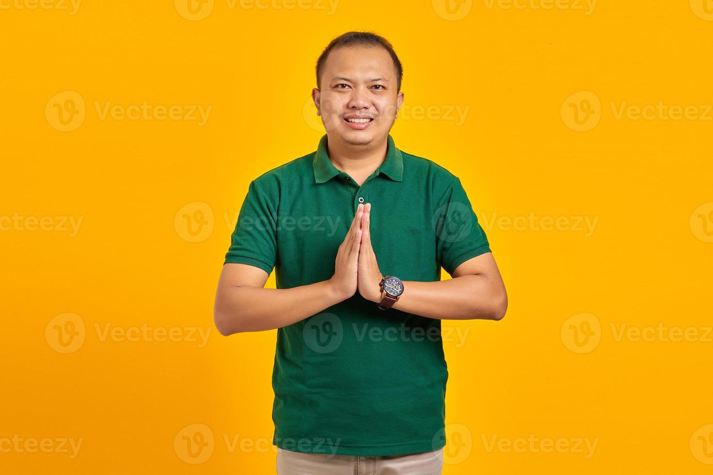 retrato de um jovem asiático sorridente, de mãos dadas, implorando sobre fundo amarelo foto