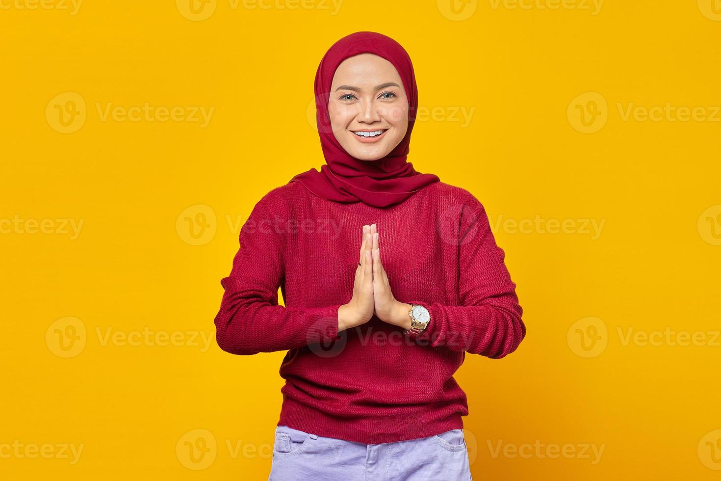 jovem mulher asiática com lenço na cabeça cumprimentando com um grande sorriso no rosto, isolado no fundo amarelo foto