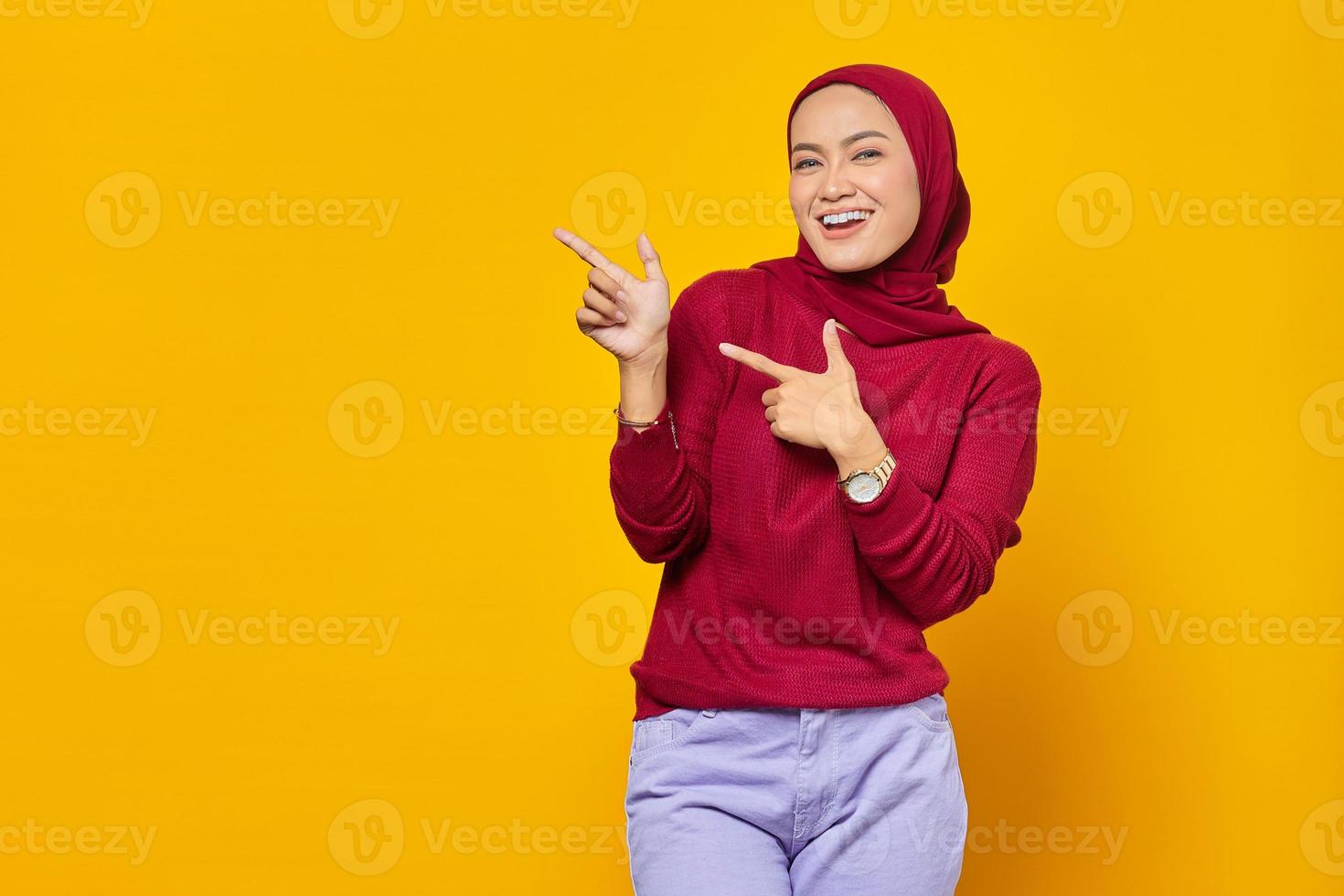 retrato de uma jovem mulher asiática sorridente apontando o dedo para o espaço da cópia em fundo amarelo foto