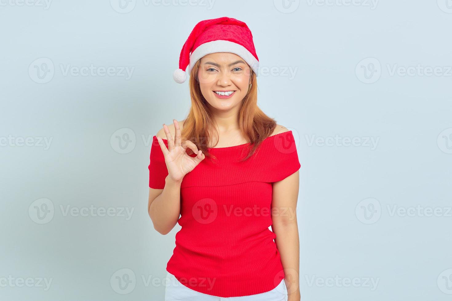 retrato de uma linda mulher asiática sorridente usando vestido de Natal e mostrando gesticulando sinal de tudo bem no fundo branco foto