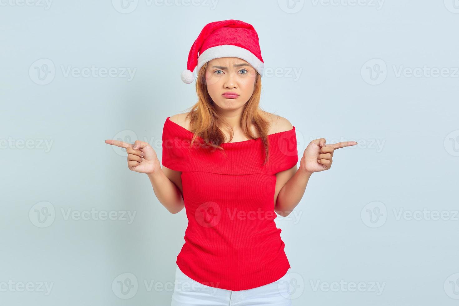 retrato de jovem asiática com vestido de natal apontando para as laterais, tendo dúvidas foto