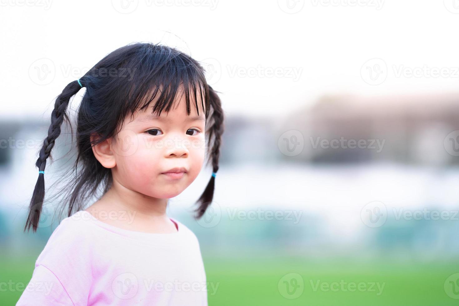 rosto de menina está se voltando para a câmera e sorrindo suavemente. criança trança duas tranças. garoto usa camiseta rosa claro. crianças de 4 a 5 anos. foto