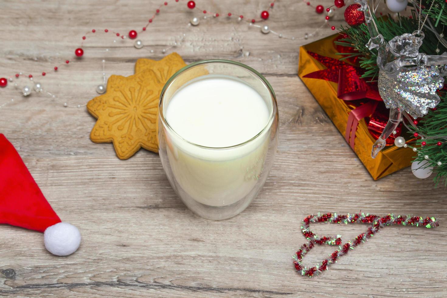 leite de natal e pão de gengibre para o papai noel. um grande copo com leite e decorações festivas. foto de uma bebida de Natal em um fundo de madeira. fechar-se