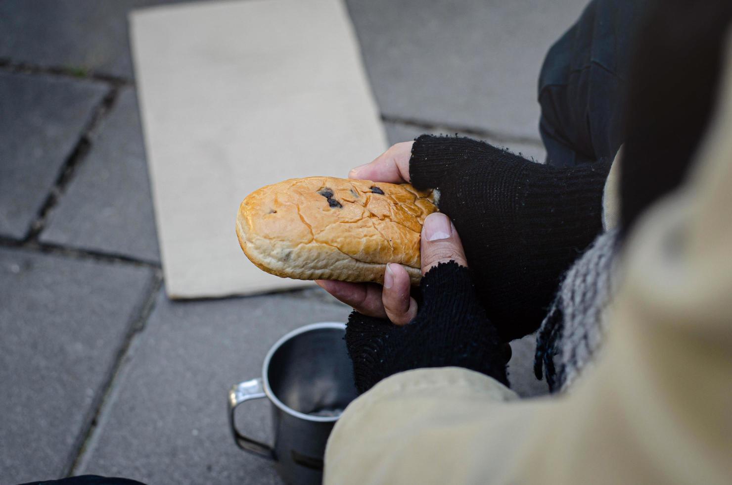 um mendigo sem-teto comendo pão e pedindo ajuda aos transeuntes. foto
