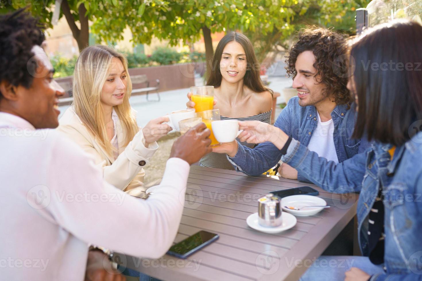 grupo multiétnico de amigos brindando com suas bebidas enquanto tomam uma bebida juntos. foto