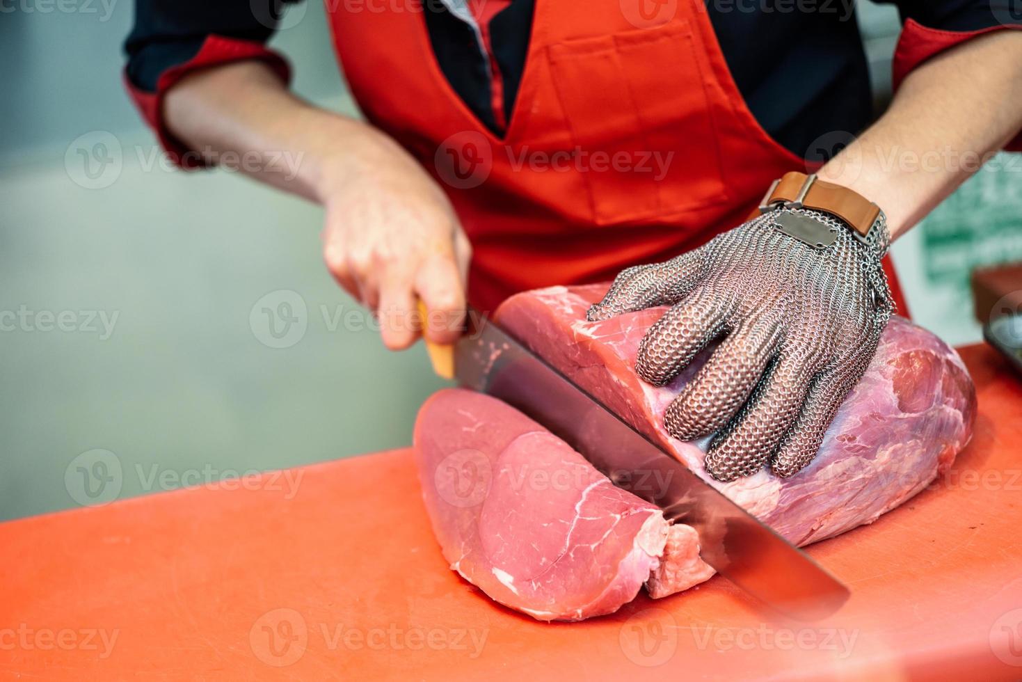 mulher cortando carne fresca em um açougue com luva de malha de segurança de metal foto