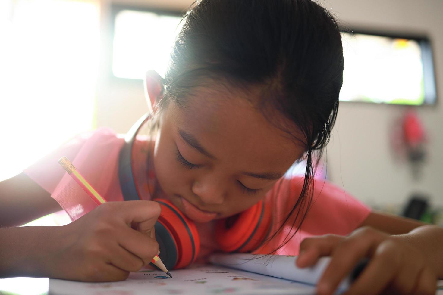 uma linda garota asiática fazendo lição de casa em sua casa durante o dia foto