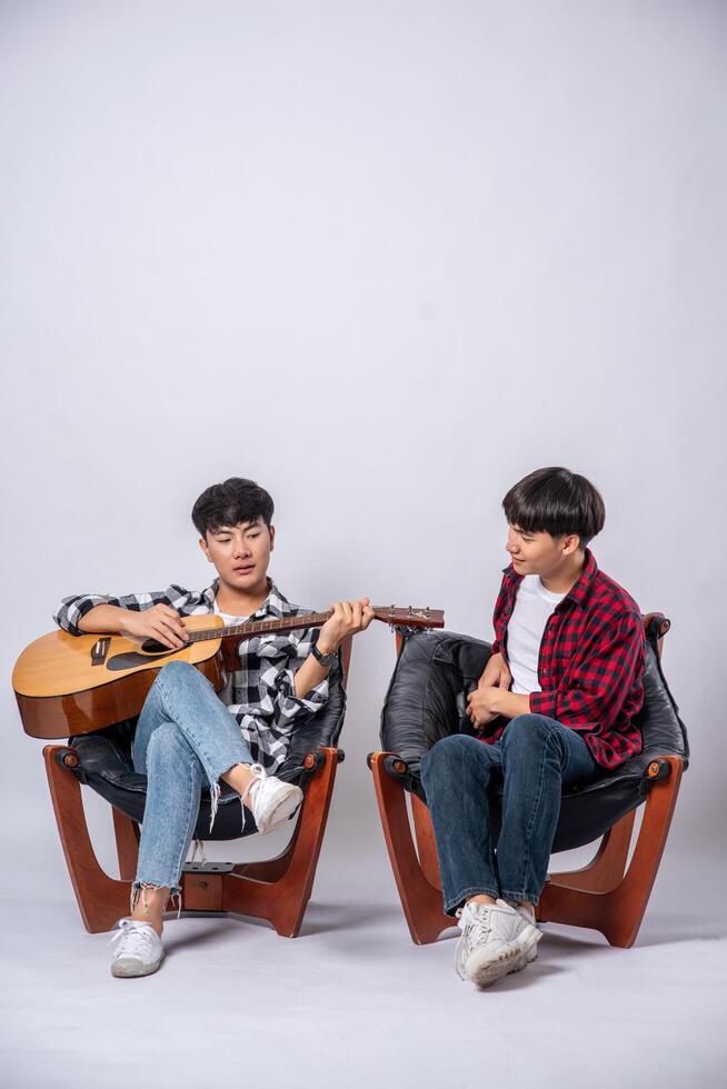 dois jovens sentaram-se em uma cadeira e tocaram violão. foto