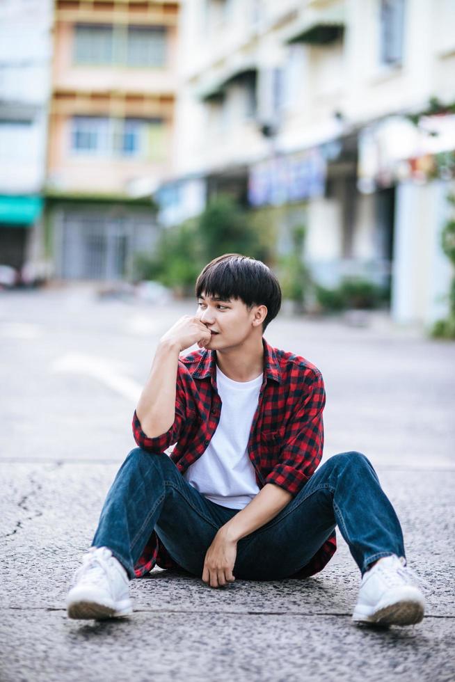um jovem com uma camisa listrada sentado na rua foto