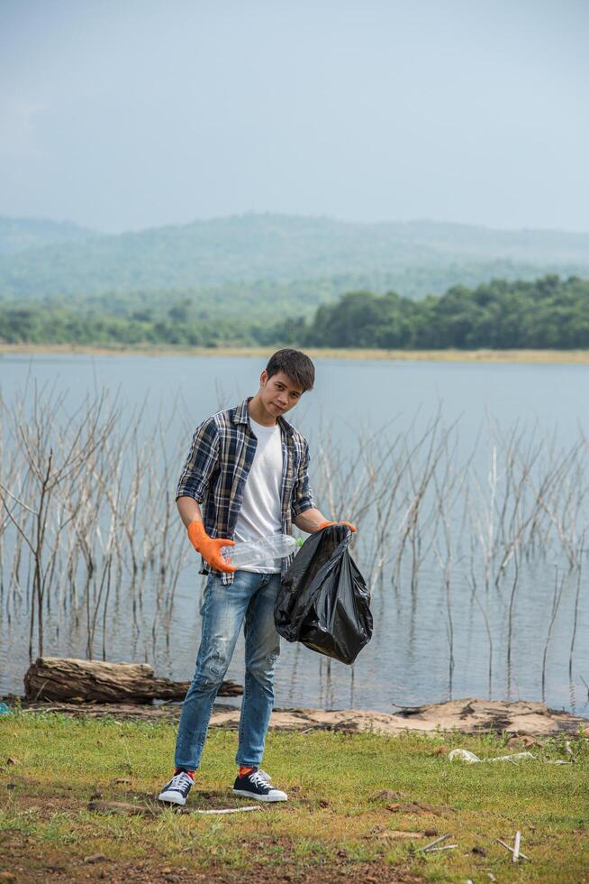 um homem usando luvas laranja, recolhendo lixo em um saco preto. foto