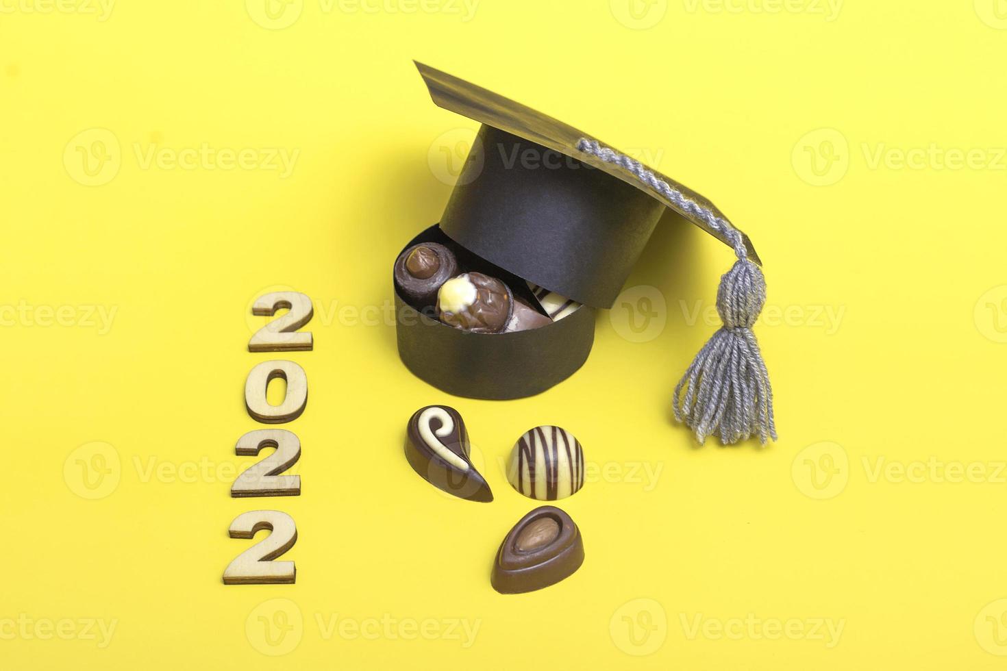 uma caixa de chocolates em forma de um chapéu de formatura. conceito do dia do chocolate. formatura 2022 em espaço de cópia de fundo amarelo foto