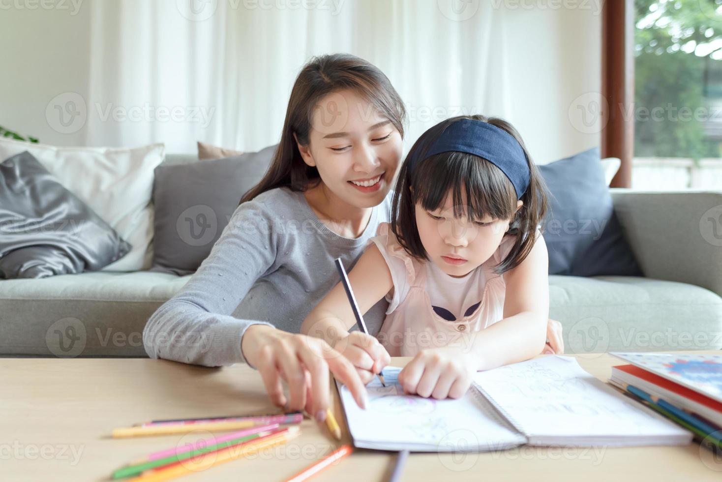 mãe asiática ensinando sua filha linda a estudar na sala de estar em casa foto