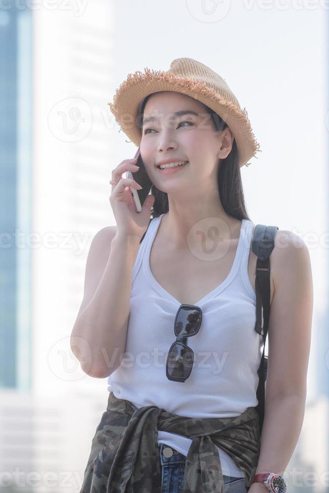 mulher linda turista solo asiático sorrindo e desfrutar de tomar via celular no centro da cidade. viagens de férias no verão. foto