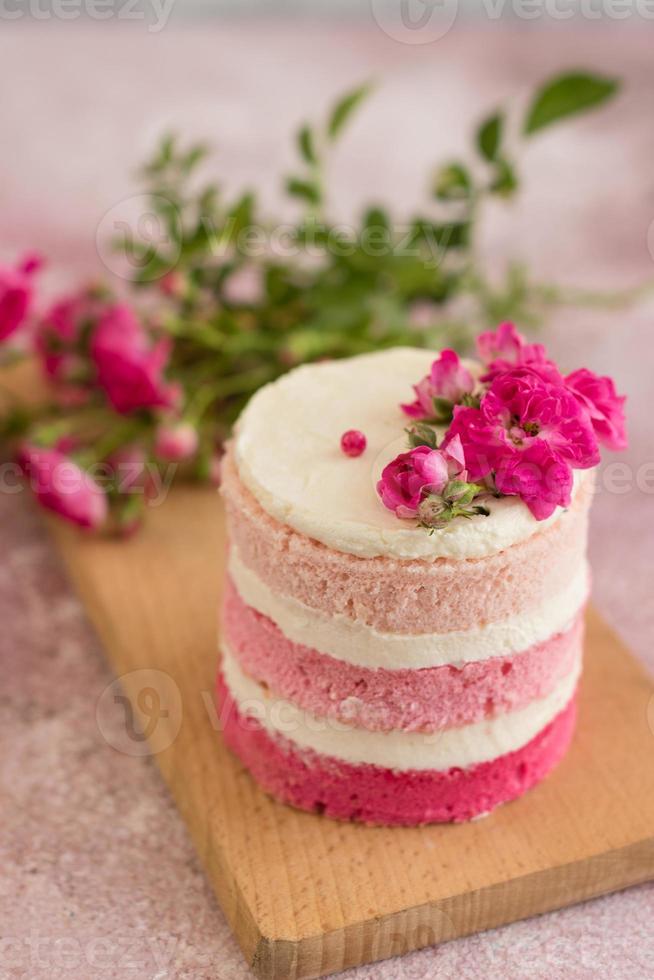 um pequeno bolo de branco e rosa decorado com flores e frutos silvestres foto