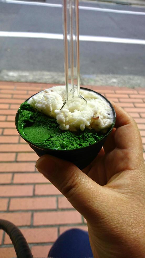 Sorvete verde e creme de baunilha com sabor de sobremesa congelada padrão na mão do copo preto segurando na madeira. foto