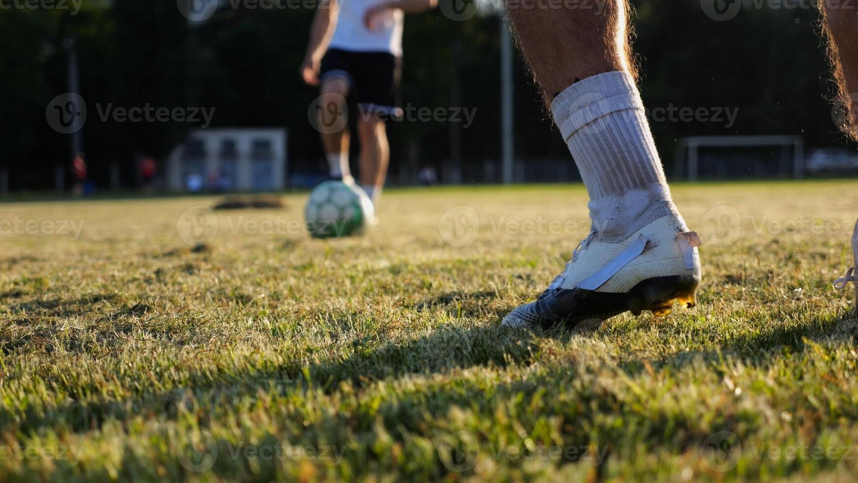 masculino pés do profissional jogadores de futebol passagem futebol bola em estádio às pôr do sol. pernas do desportistas chutando bola às verde campo. jovem homens Treinamento às Prado. conceito do uma estilo livre futebol. lento foto