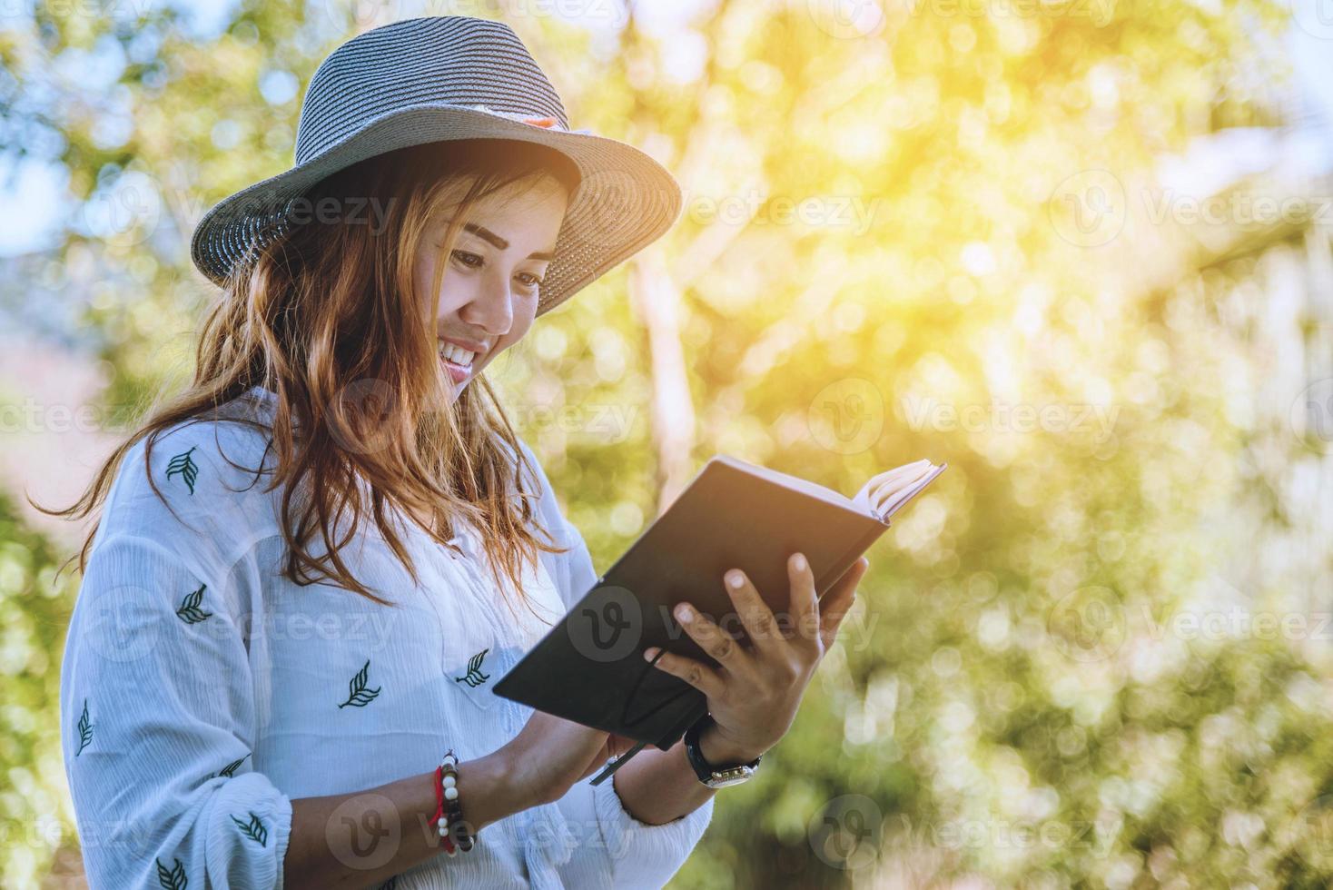 mulher asiática viajar natureza. viajar relaxar. estudo ler um livro. educação na natureza escreva uma nota em um parque público no verão. Na Tailândia foto