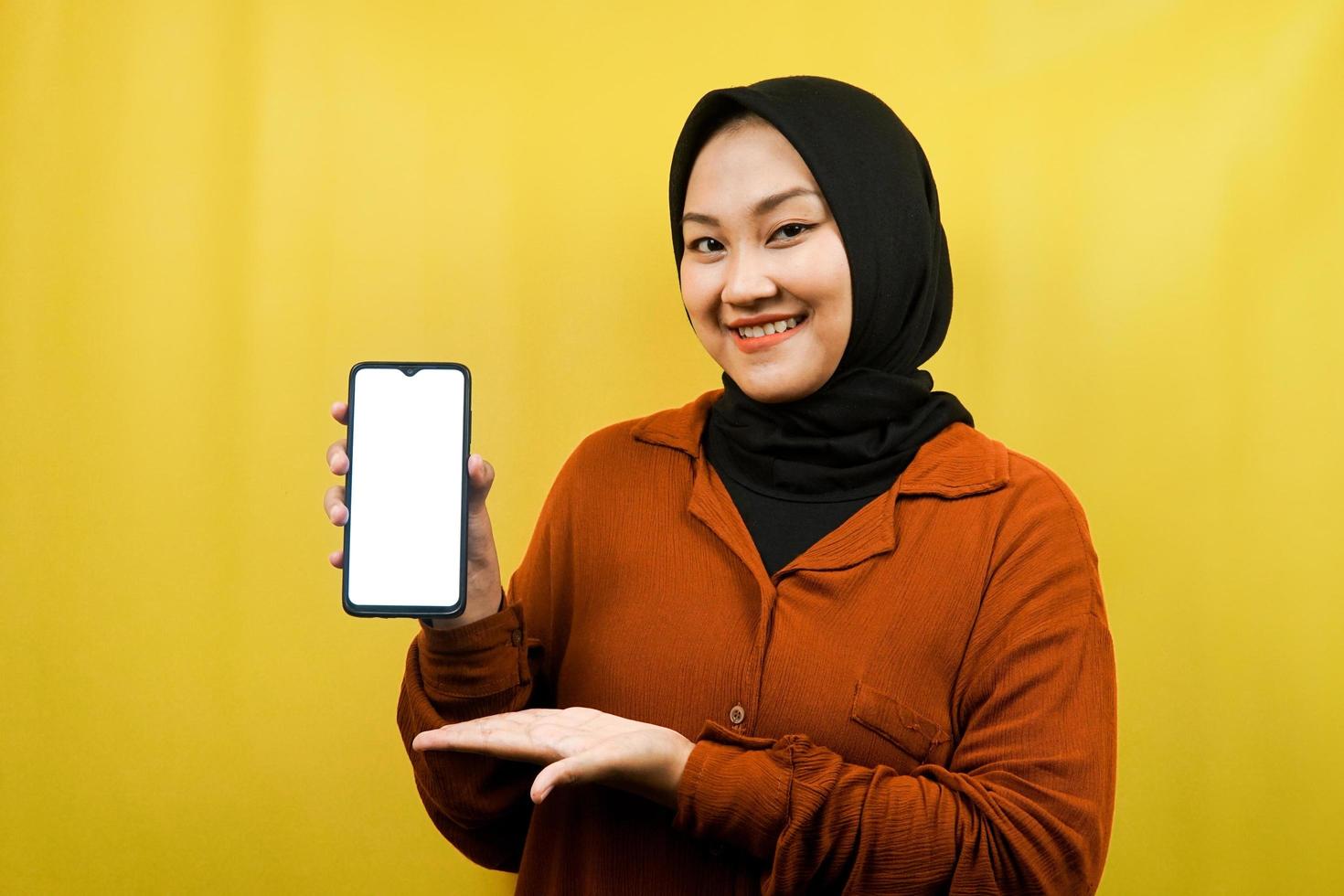 bela jovem muçulmana asiática segurando smartphone com tela branca ou em branco, promovendo app, promovendo algo, isolado, conceito de publicidade foto