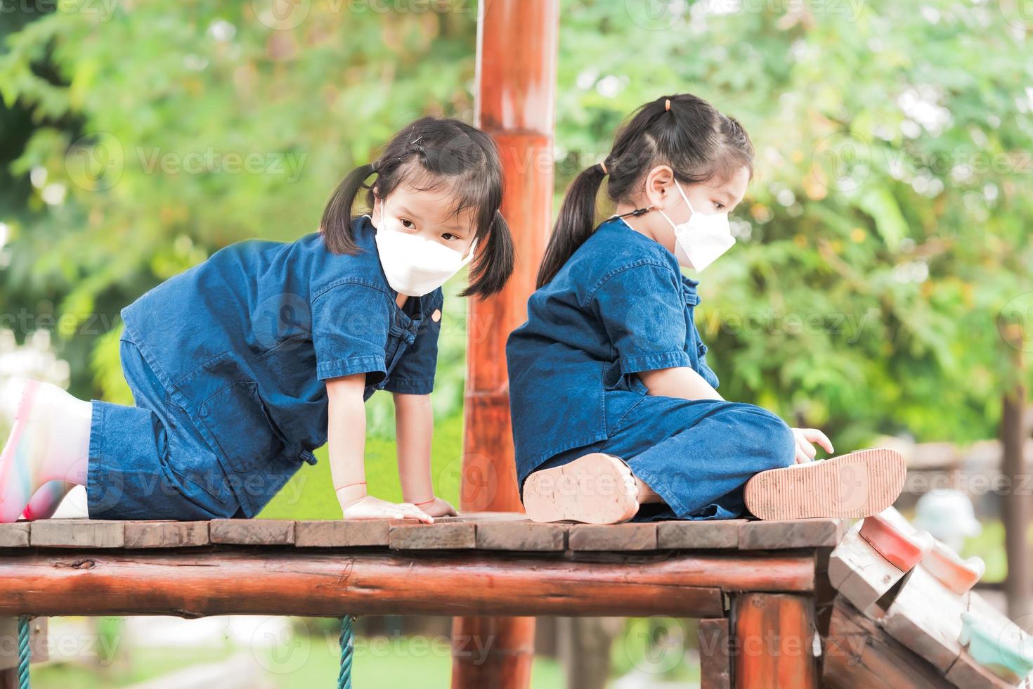 duas garotas usando máscara branca estão brincando de escalada em equipamentos de madeira do recreio. para prevenir vírus e pequenas poeiras tóxicas que são a poluição do ar pm2.5. foto