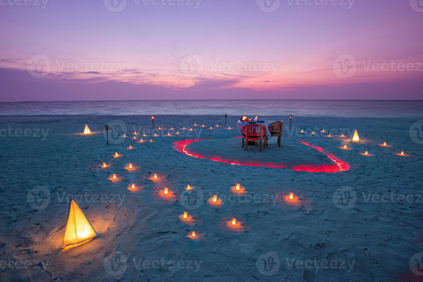 linda mesa preparada para uma refeição romântica na praia com lanternas e cadeiras e flores com velas e céu e mar ao fundo. jantar na praia ao pôr do sol foto