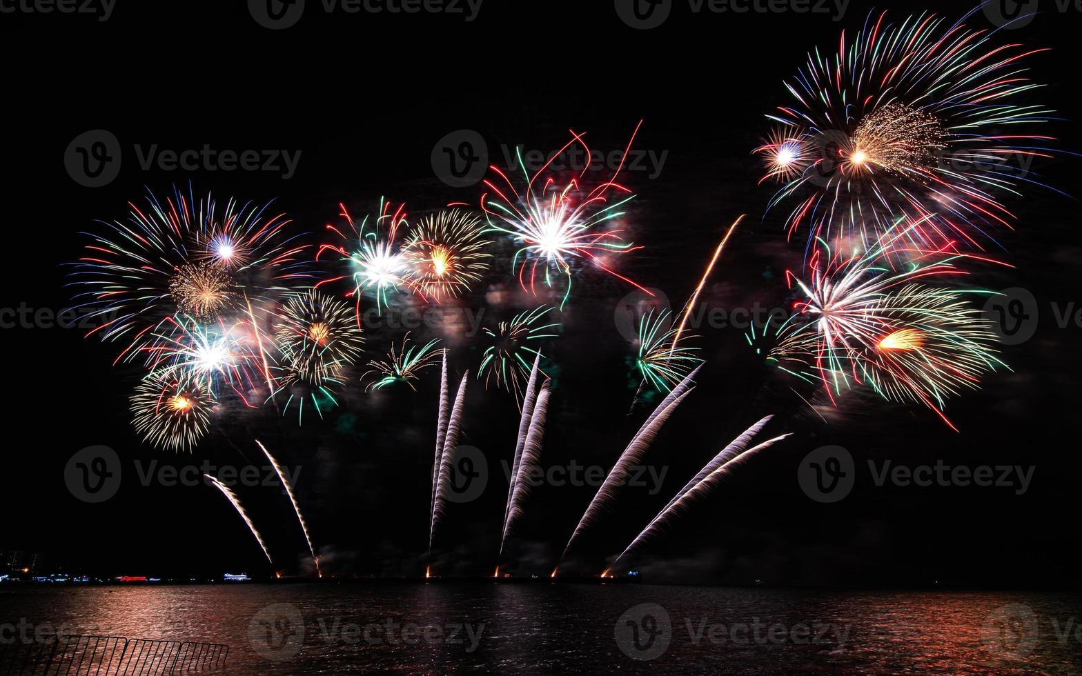 incríveis e lindos fogos de artifício coloridos na noite de celebração, mostrando na praia do mar com reflexo de várias cores na água foto