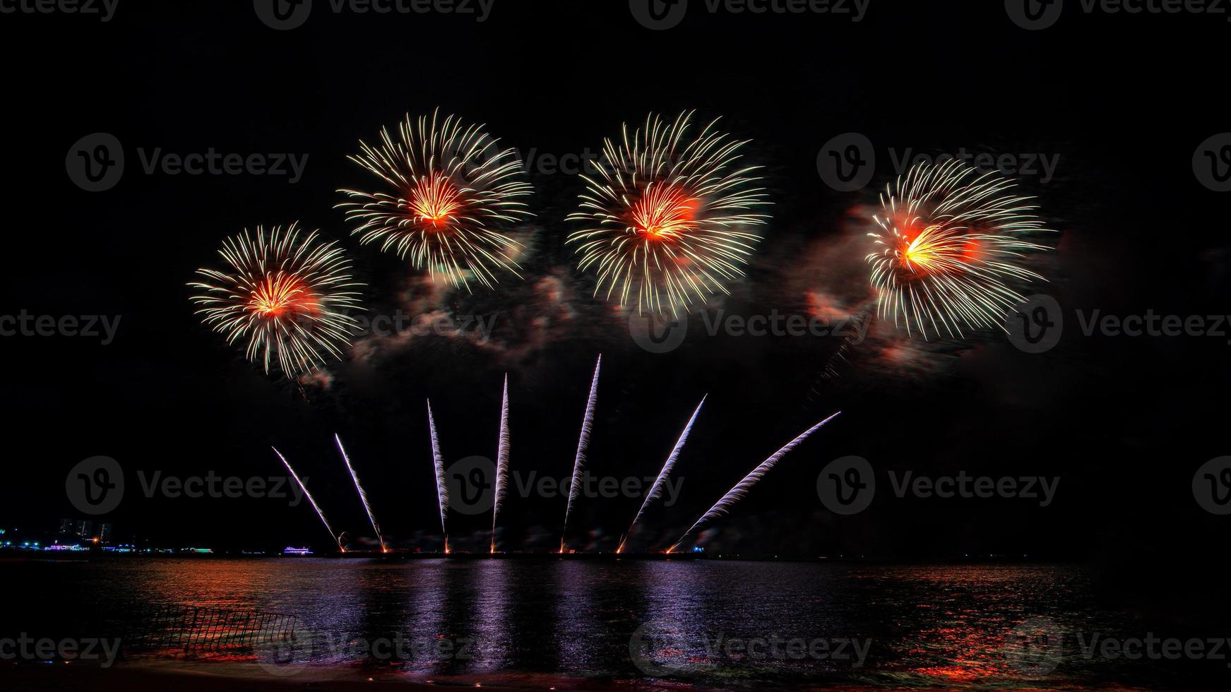 incríveis e lindos fogos de artifício coloridos na noite de celebração, mostrando na praia do mar com reflexo de várias cores na água foto