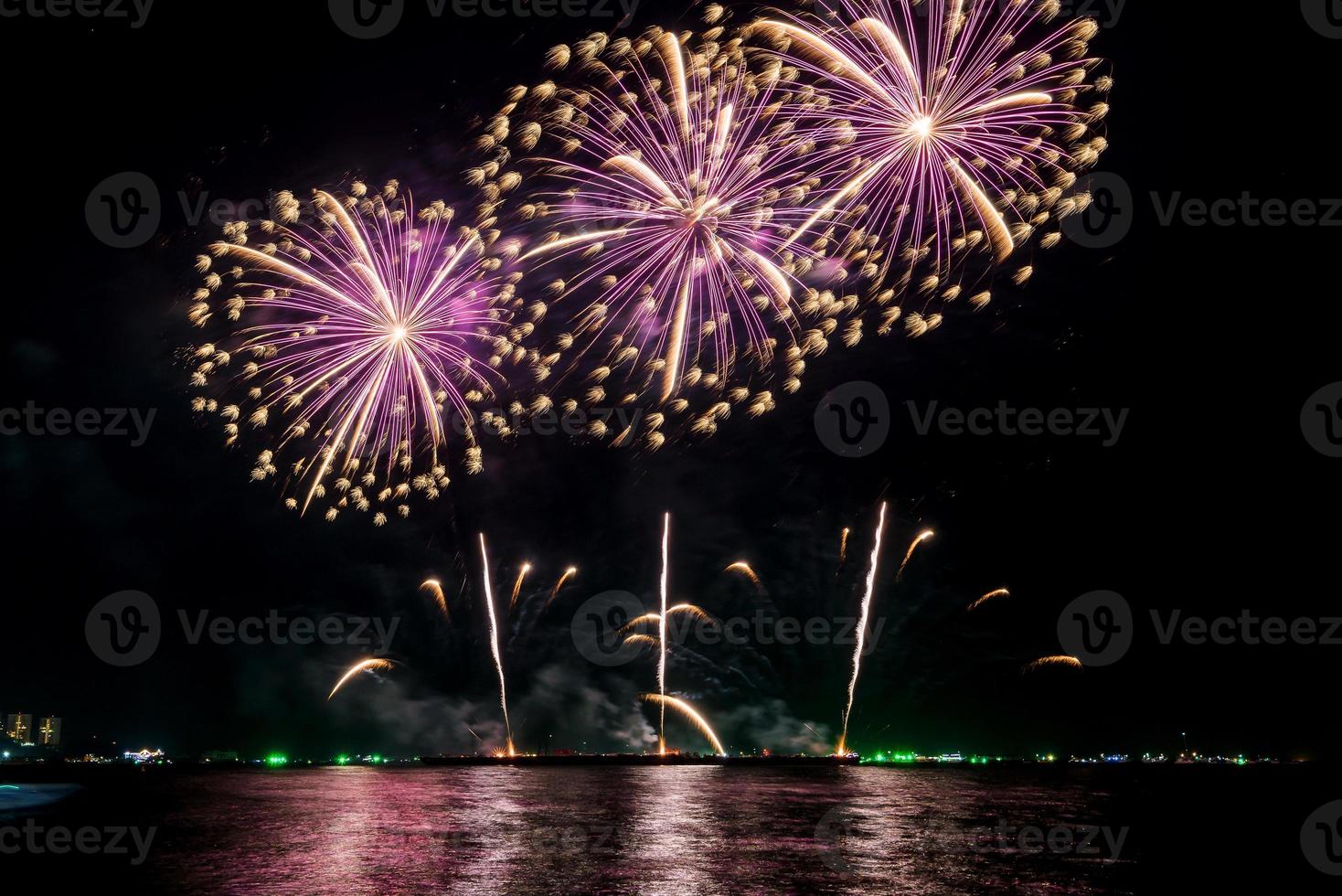 incríveis e lindos fogos de artifício coloridos na noite de celebração, mostrando na praia do mar com reflexo de várias cores na água foto