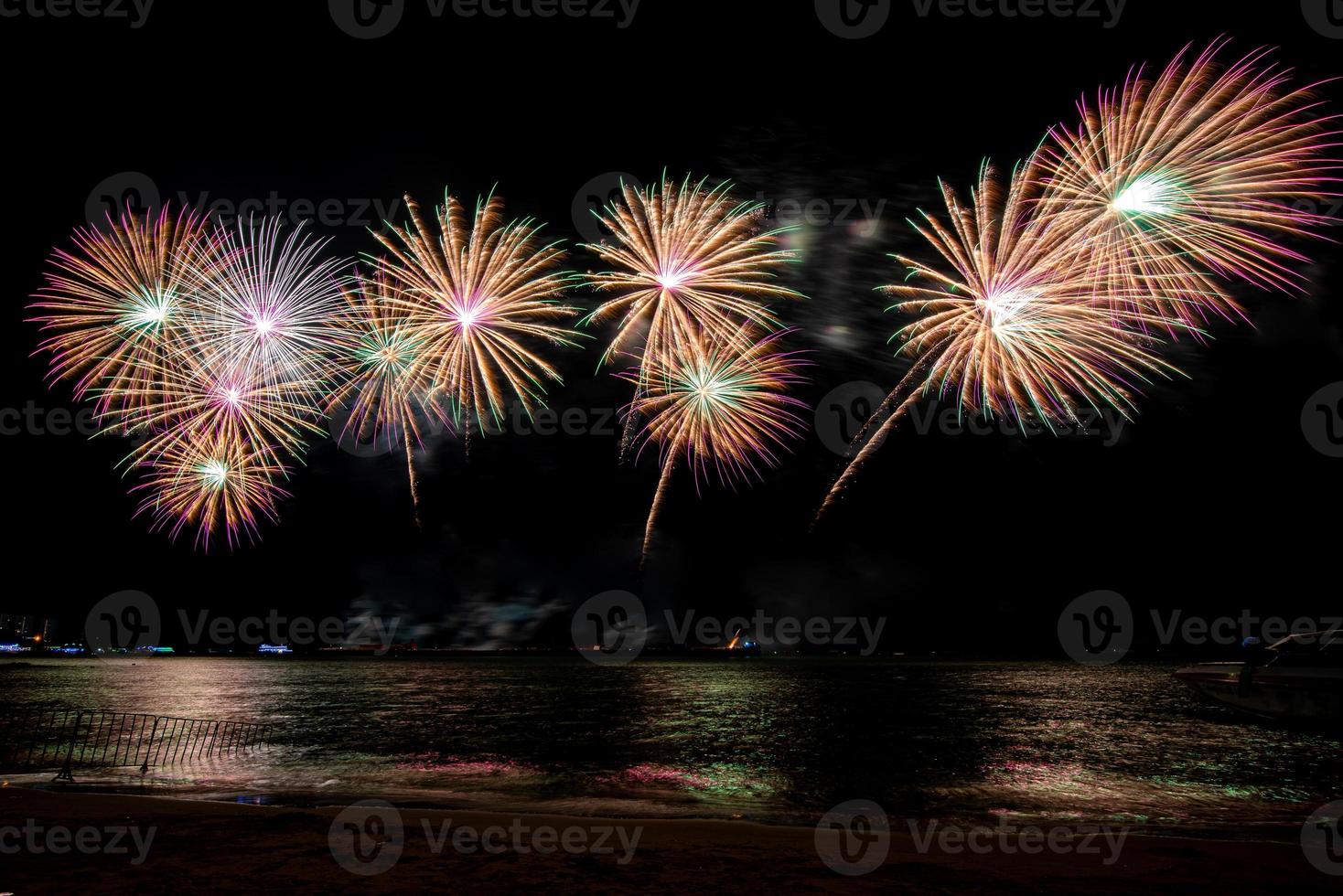 incríveis e lindos fogos de artifício coloridos na noite de celebração, mostrando na praia do mar com reflexo de várias cores na água foto