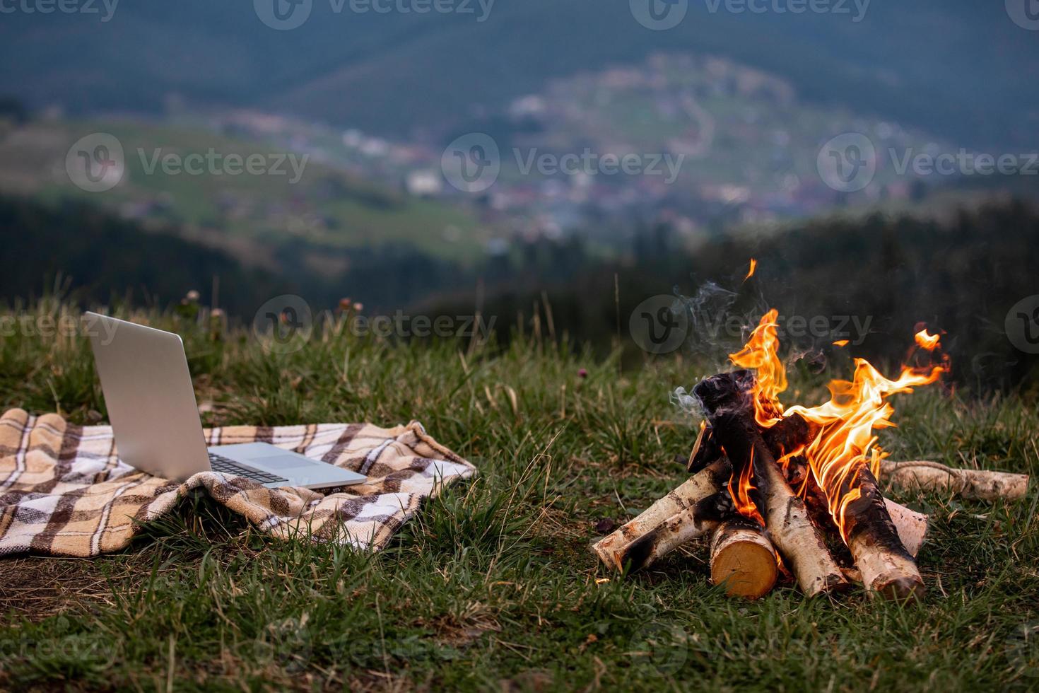 laptop na manta perto da fogueira. atrás do fundo da montanha. freelancer por natureza. copie o espaço foto