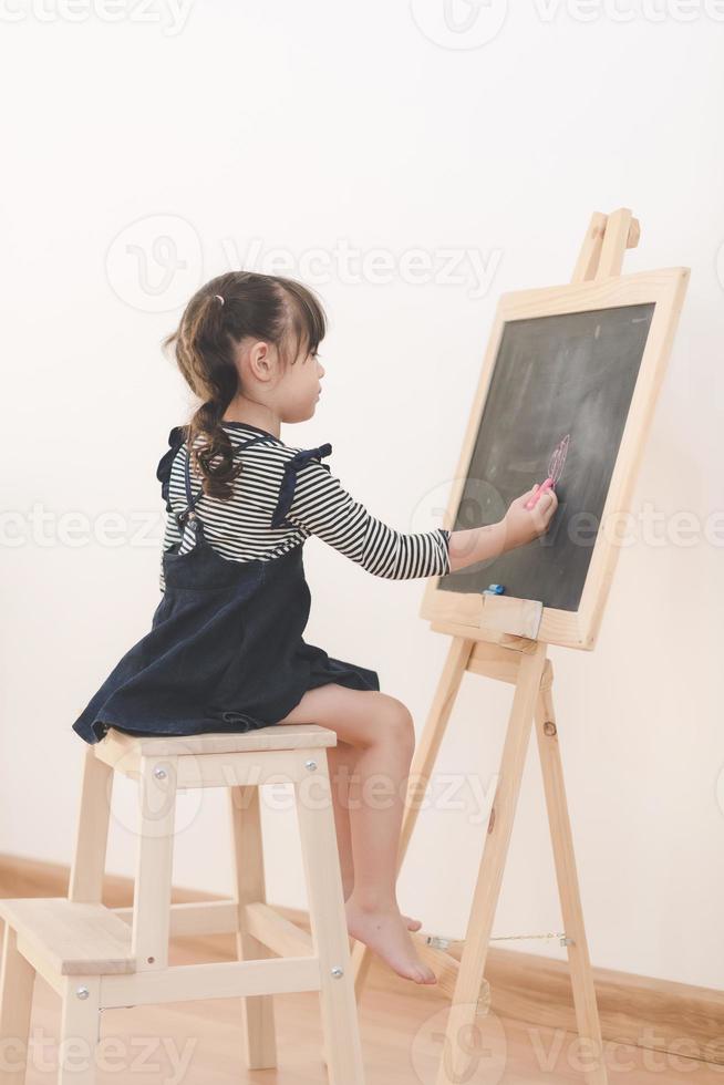 criança feliz menina asiática desenhar desenhos animados com giz na lousa para aprender em casa. foto para a educação infantil e o conceito de estudo escolar.