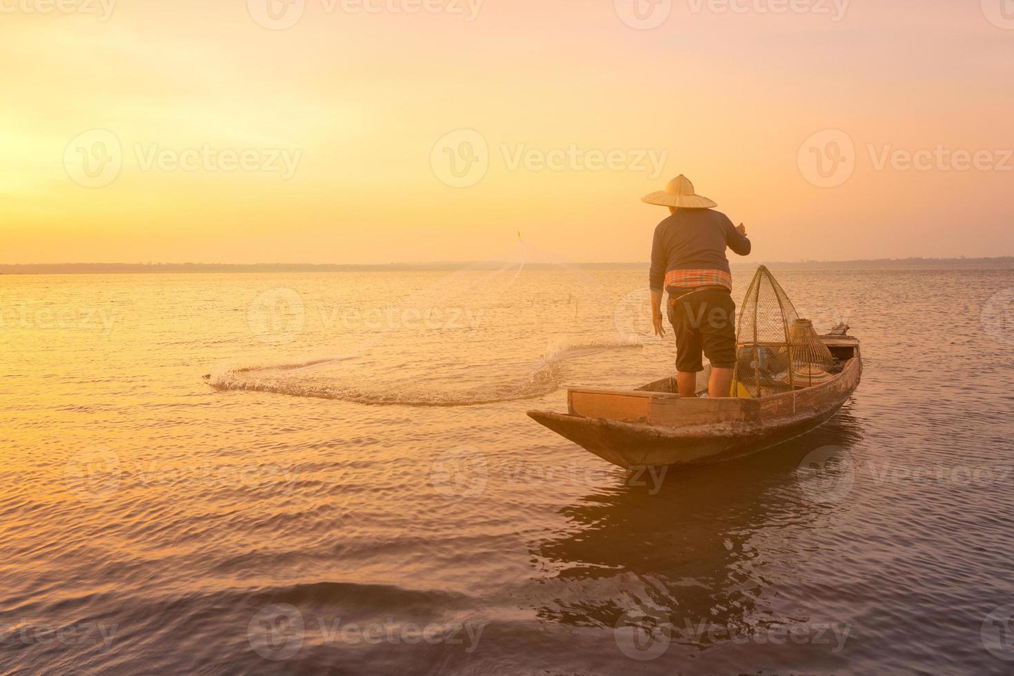 pescador asiático com barco de madeira jogando uma rede para pegar peixes de água doce no rio da natureza no início durante o nascer do sol foto